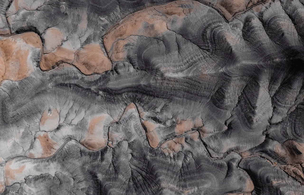 Aerial view of eroded rock formations showing banded grey and ochre layers