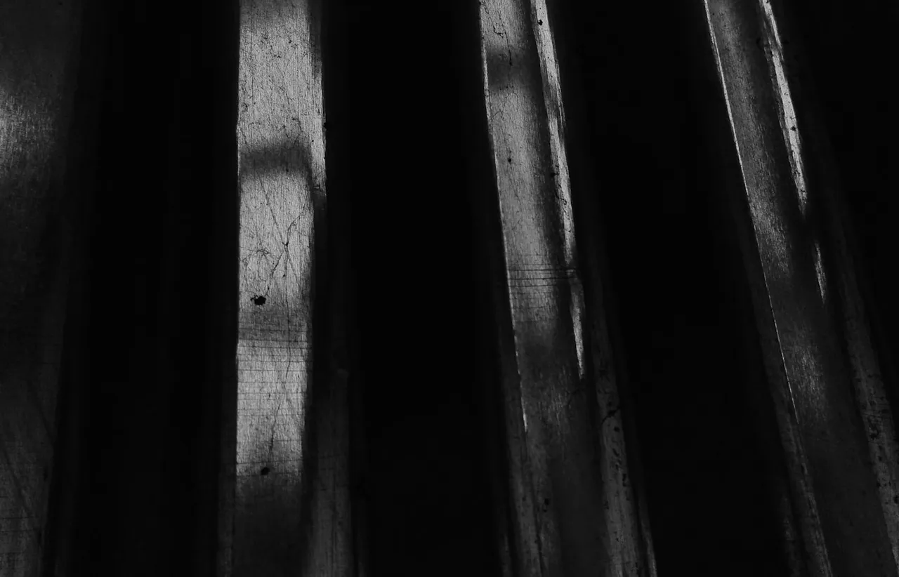 Near black close up of corrugated metal sheeting, its vertical ridges catching narrow strips of pale light