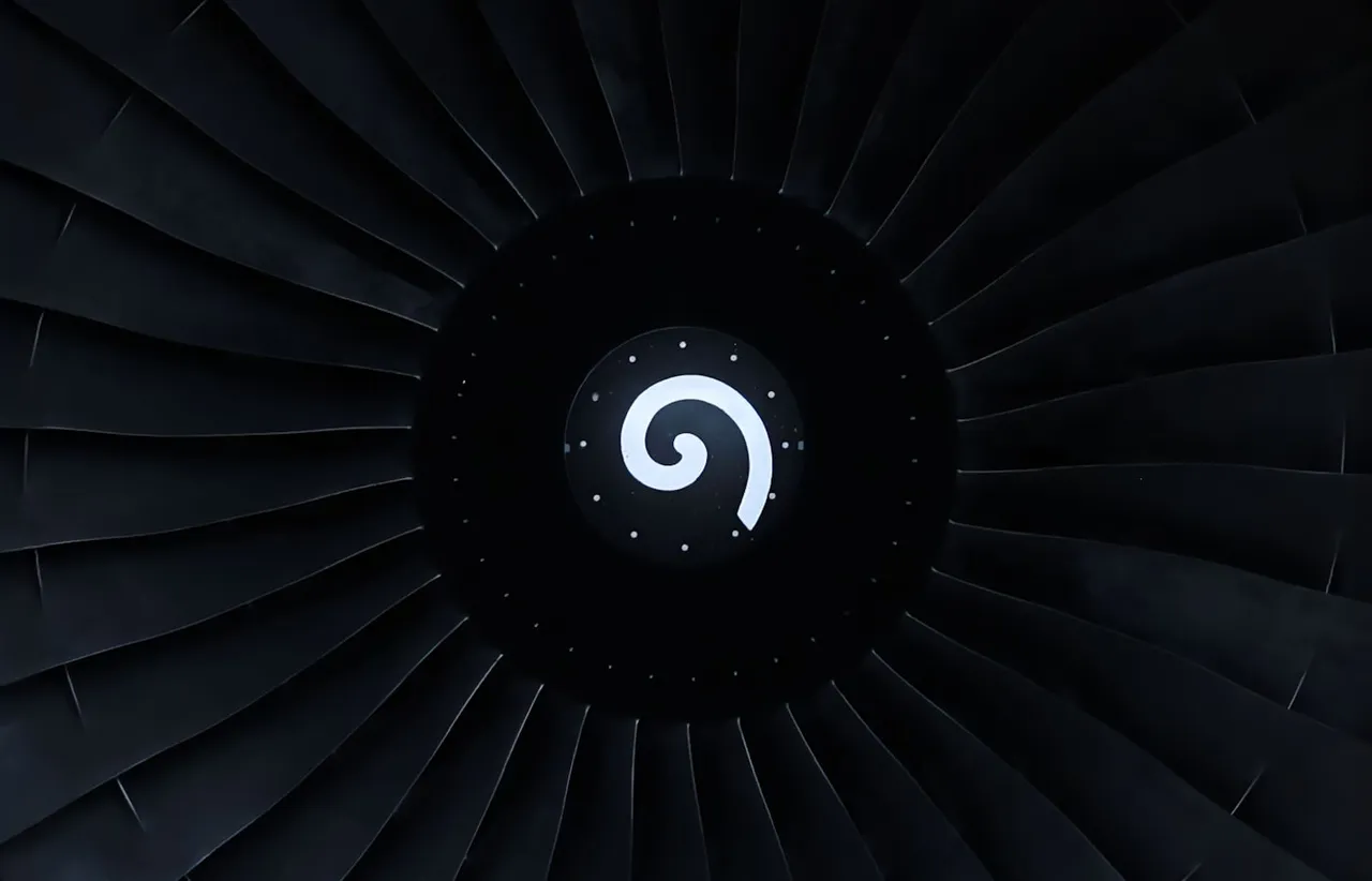 Head on view of a jet engine fan in near darkness with identical curved turbine blades radiating from a marked black hub